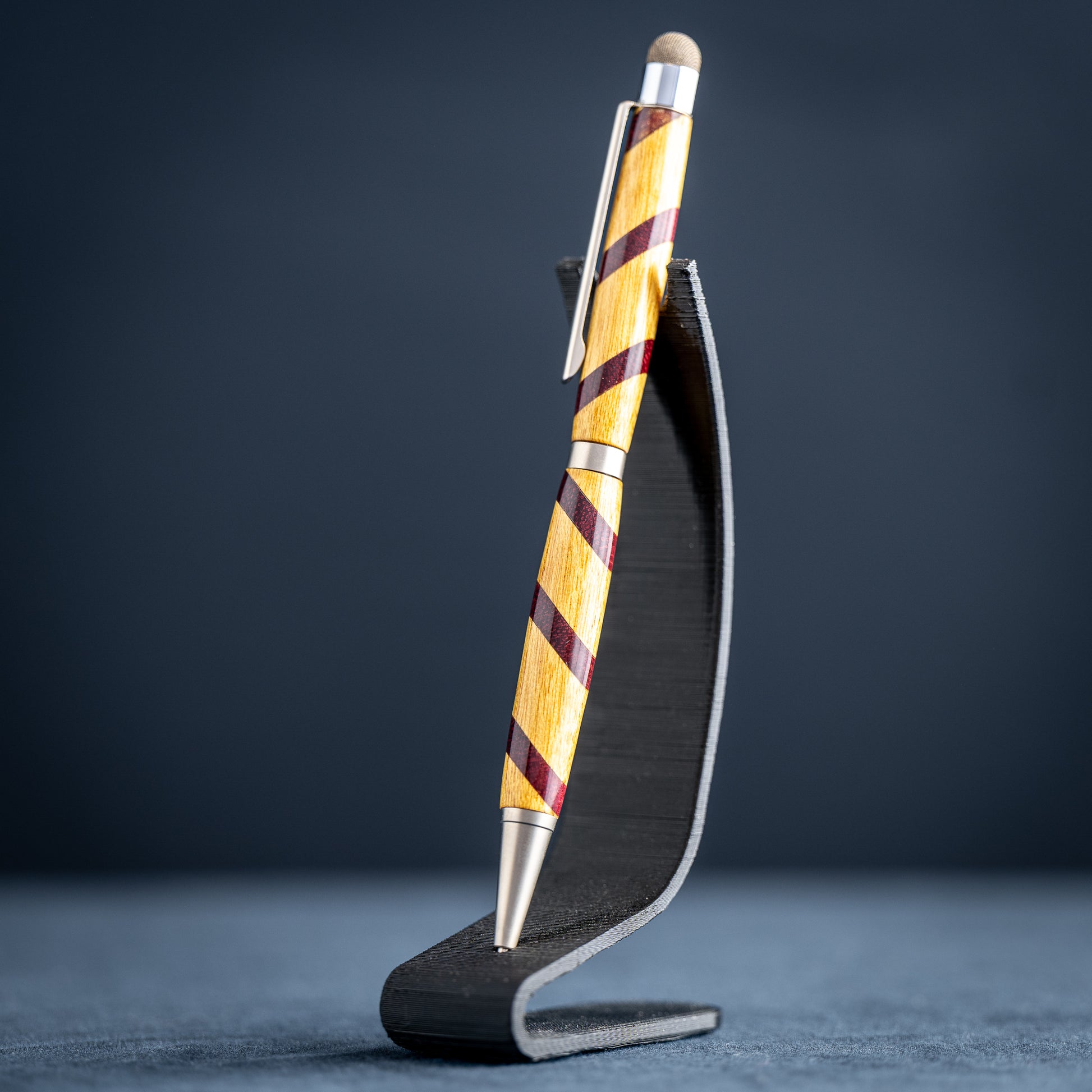 Handmade purple heart and canary wood ballpoint twist pen with stylus on a dark stand against a dark background.