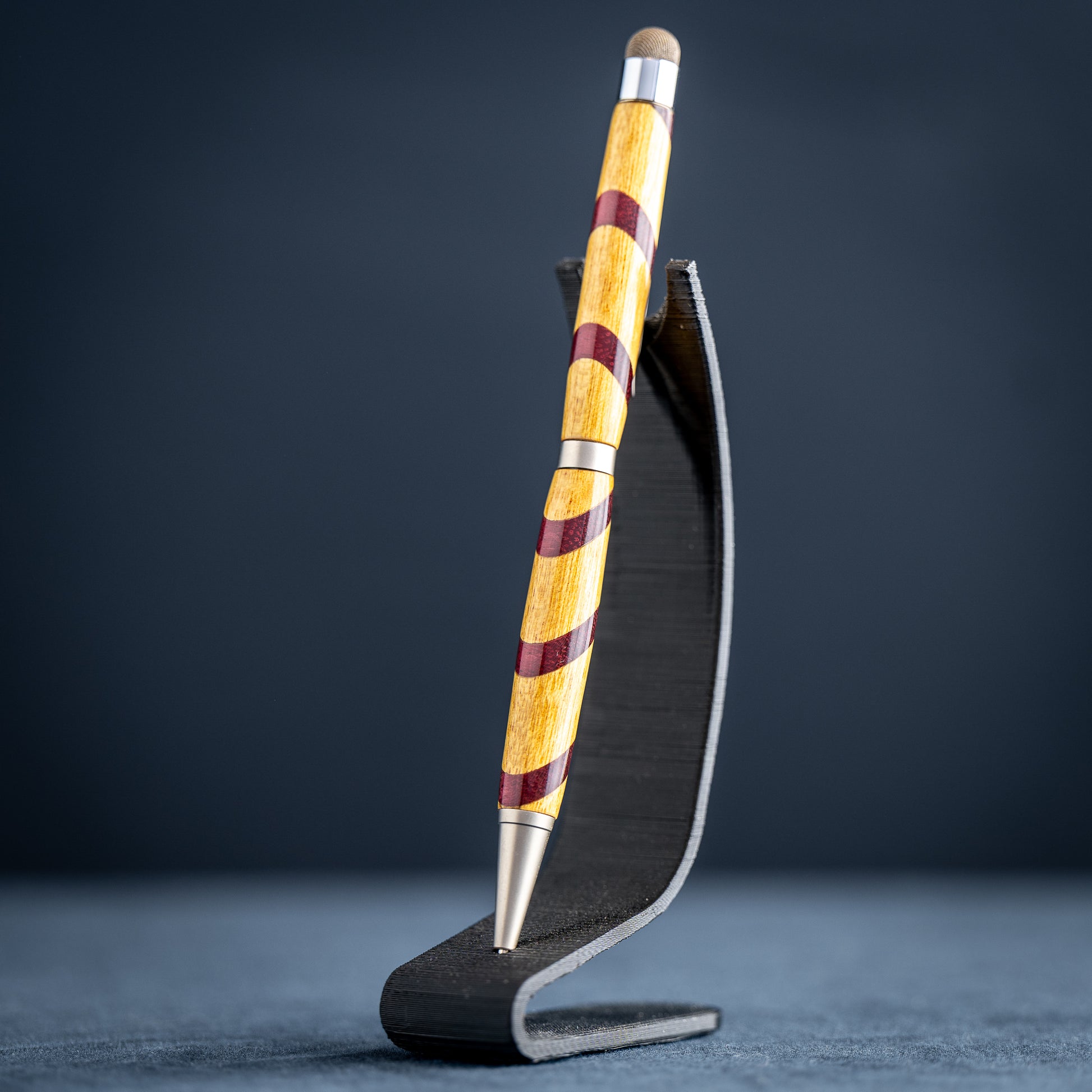 Handmade purple heart and canary wood ballpoint twist pen with stylus on a dark stand against a dark background.