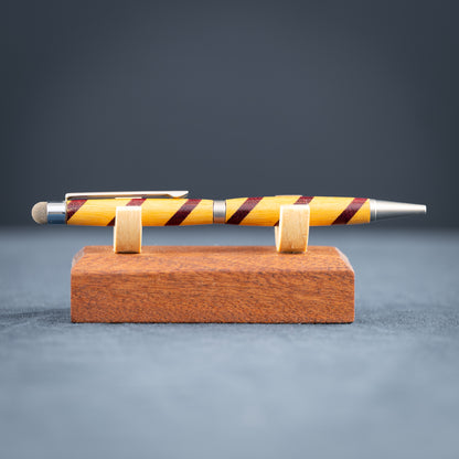 Handmade purple heart and canary wood ballpoint twist pen with stylus on a wooden stand against a dark background.