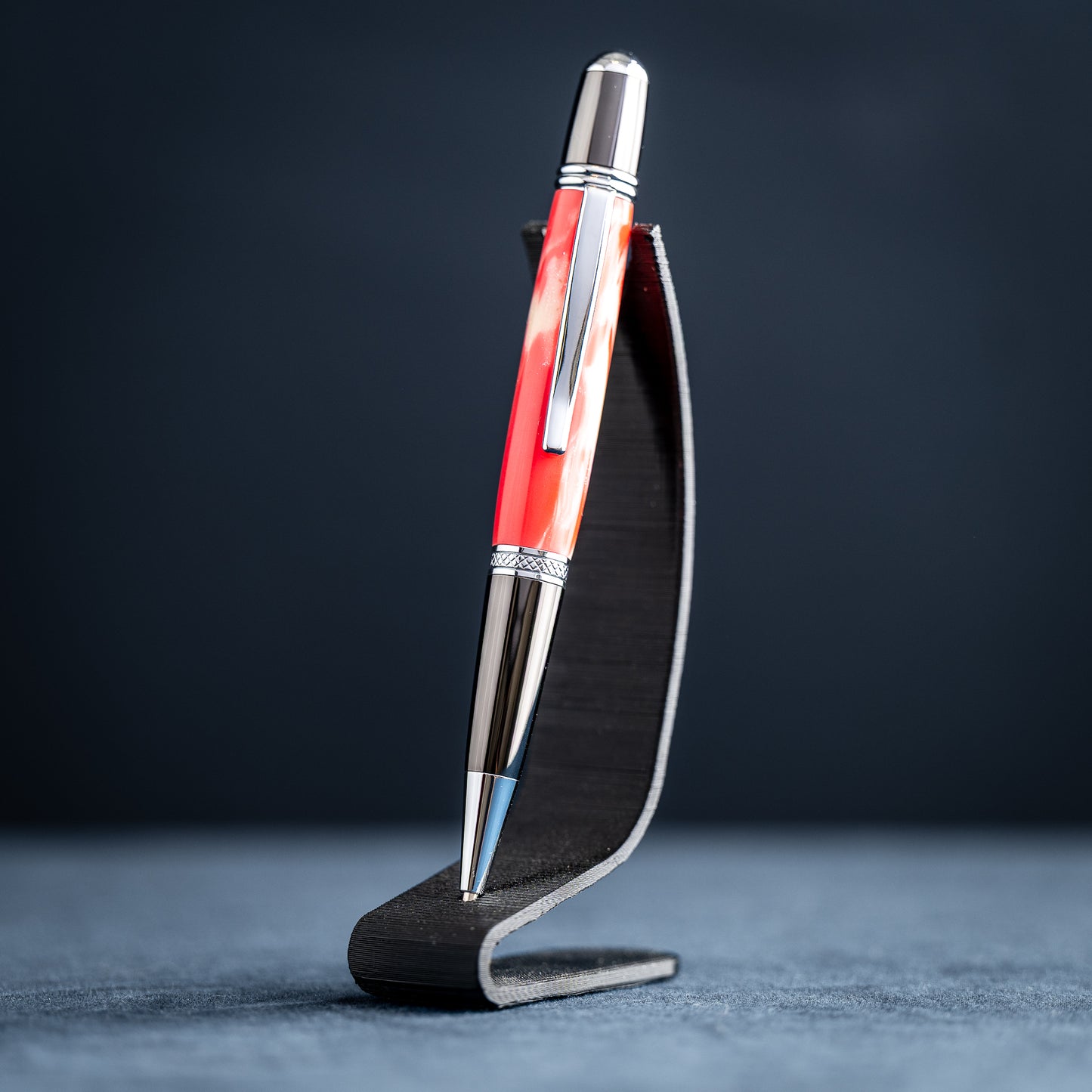 Handmade red and white resin ballpoint pen on a dark stand against a dark background.