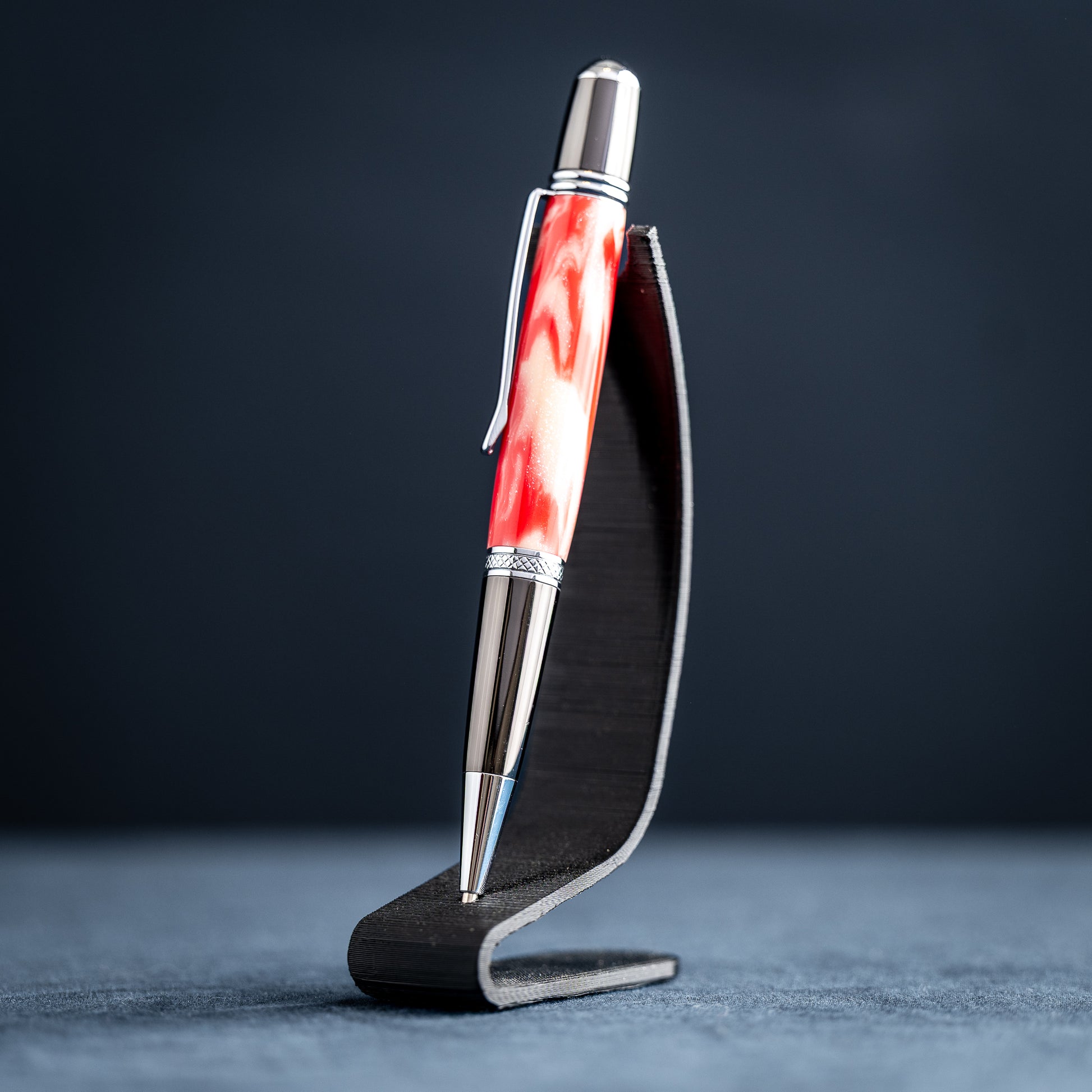 Handmade red and white resin ballpoint pen on a dark stand against a dark background.