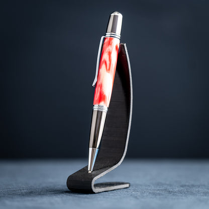 Handmade red and white resin ballpoint pen on a dark stand against a dark background.