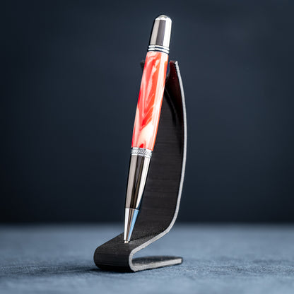 Handmade red and white resin ballpoint pen on a dark stand against a dark background.