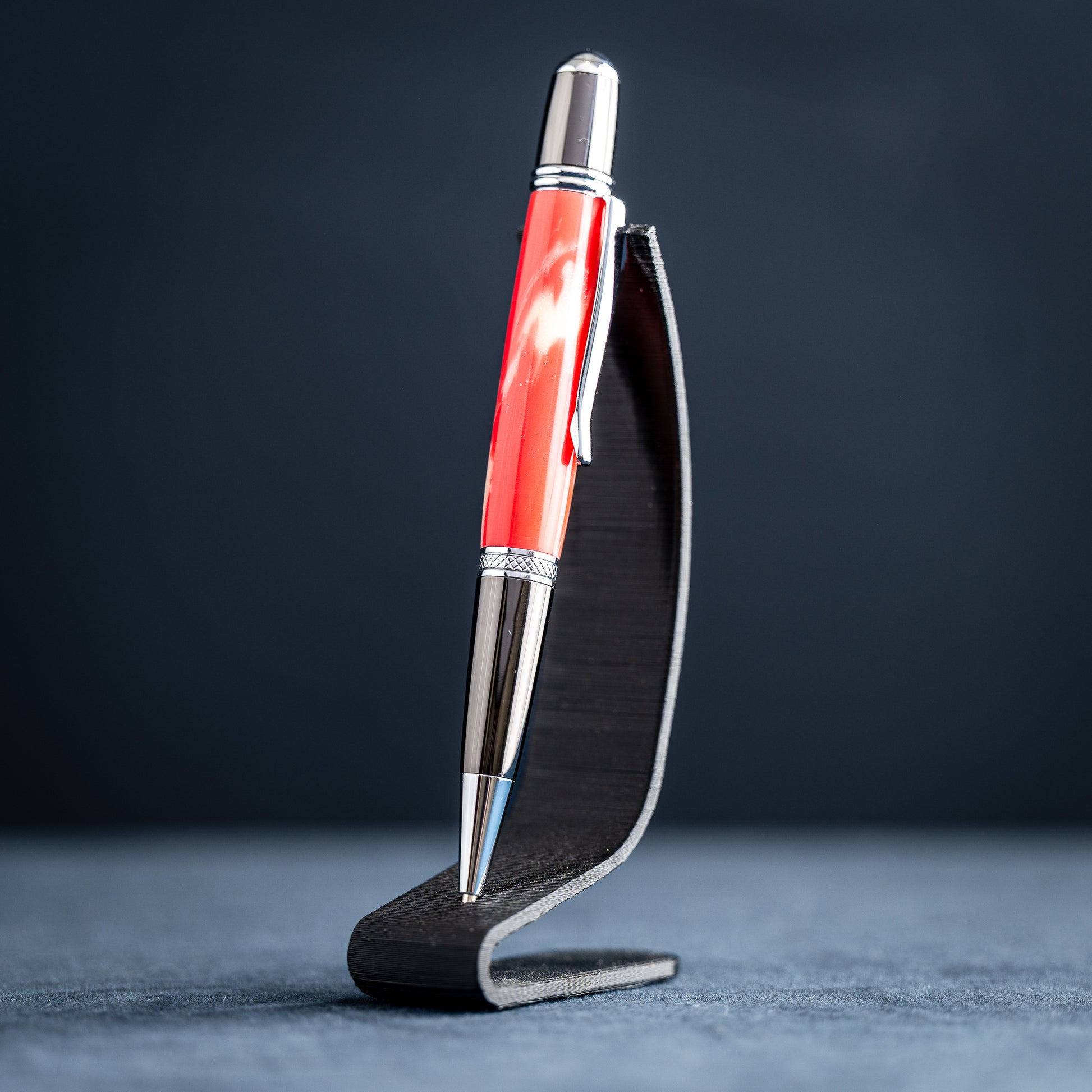 Handmade red and white resin ballpoint pen on a dark stand against a dark background.