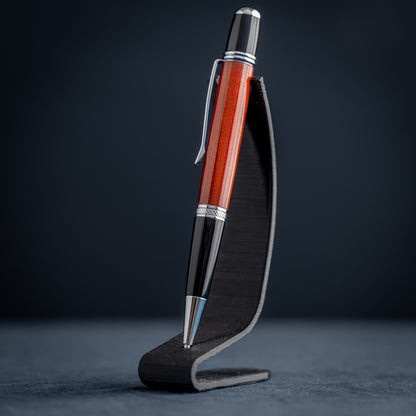 Handmade Redheart wooden ballpoint pen on a dark stand against a black background.