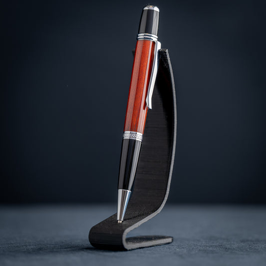 Handmade Redheart wooden ballpoint pen on a dark stand against a black background.