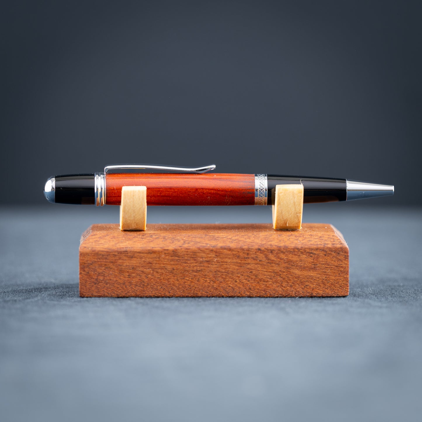 Handmade Redheart wooden ballpoint pen on a wooden stand against a black background.