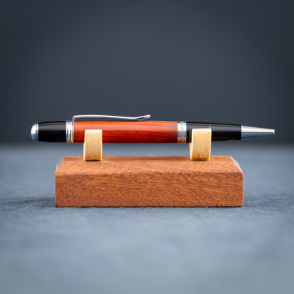 Handmade Redheart wooden ballpoint pen on a wooden stand against a black background.
