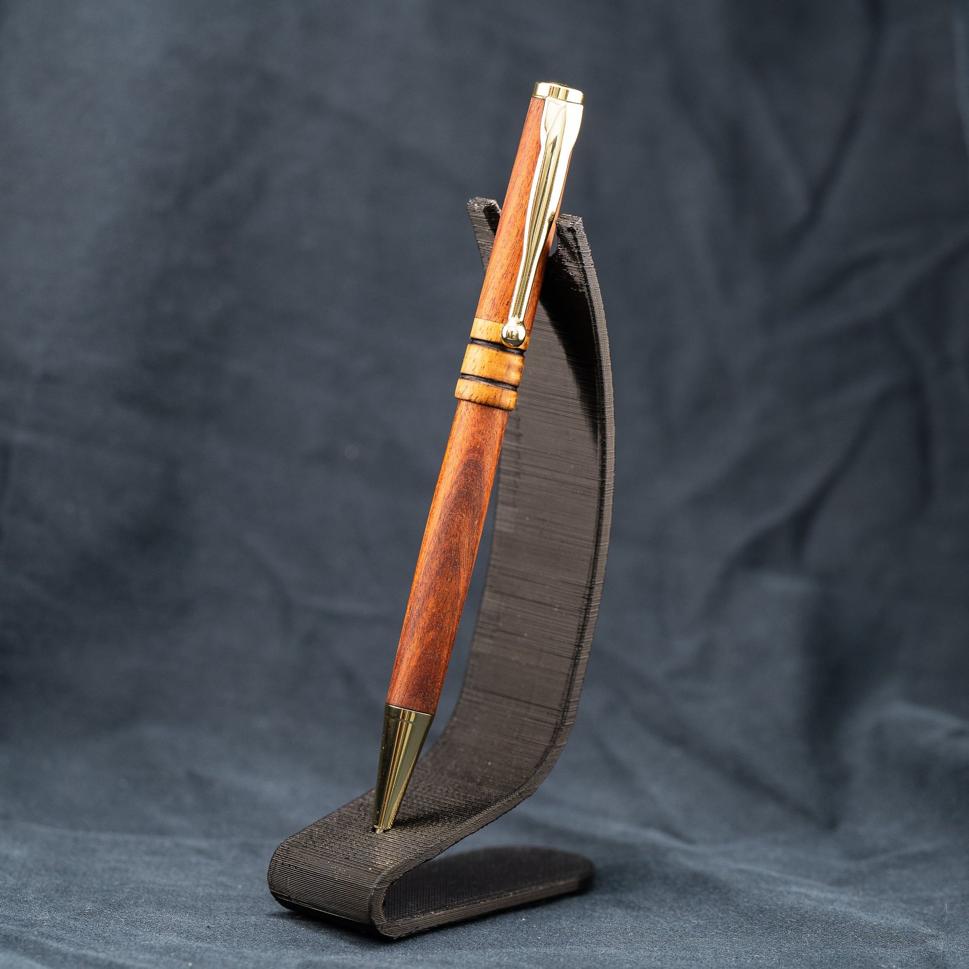 A handmade wooden twist pen made of Bolivian Rosewood and Curly Narra wood. The pen has black ink and gold plating.