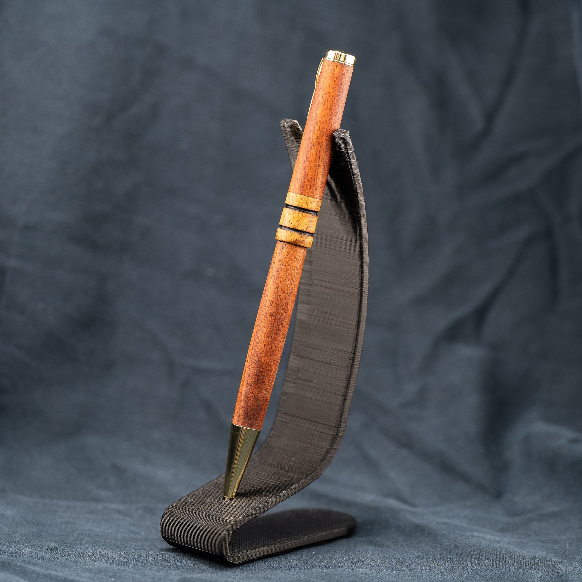 A handmade wooden twist pen made of Bolivian Rosewood and Curly Narra wood. The pen has black ink and gold plating.