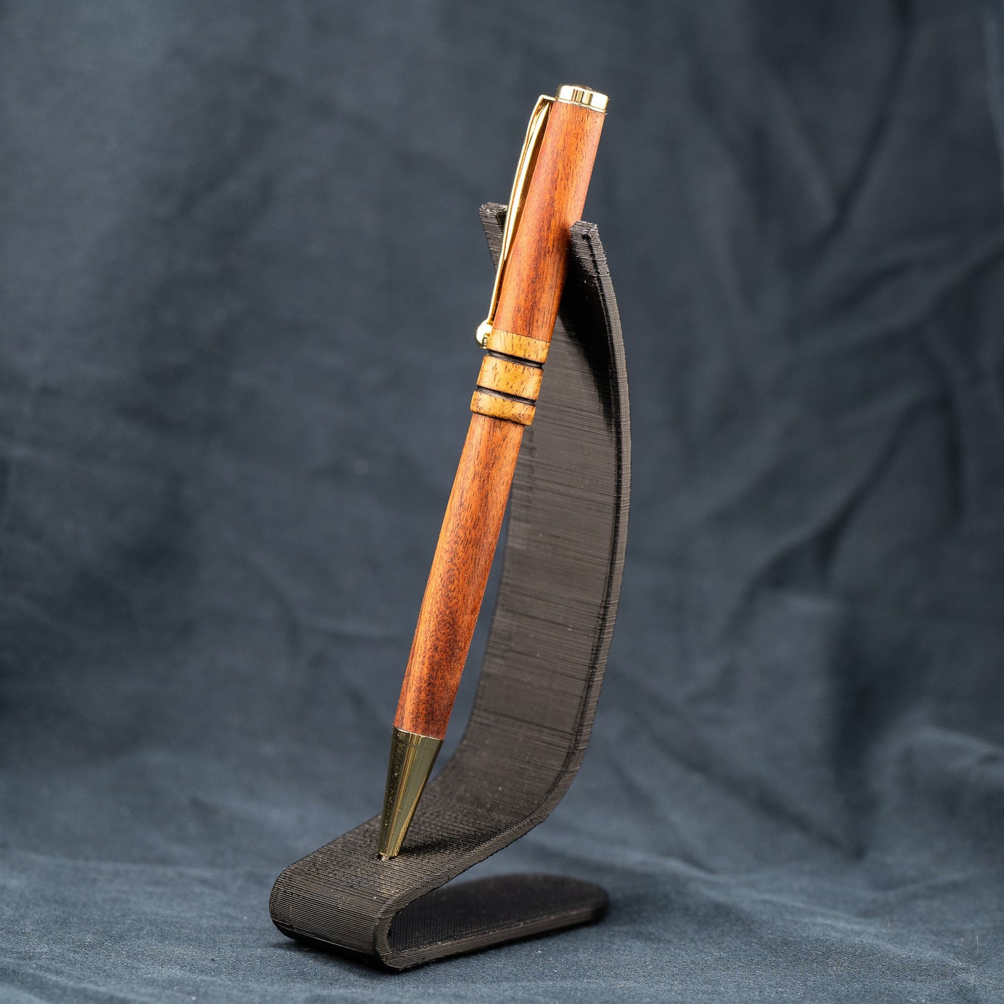 A handmade wooden twist pen made of Bolivian Rosewood and Curly Narra wood. The pen has black ink and gold plating.