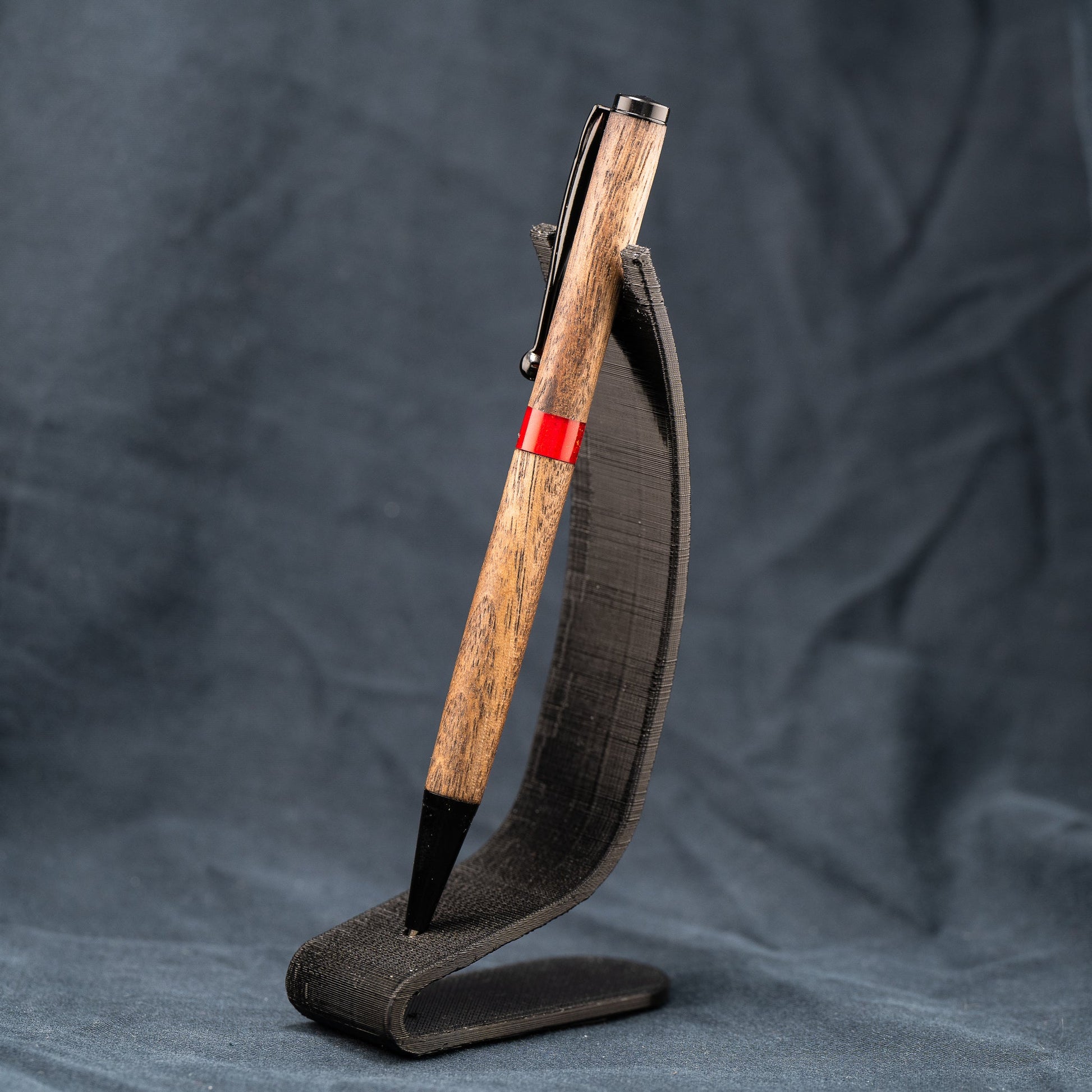 A handmade wooden twist pen made of Walnut wood and a custom red resin center band. The pen has black ink and black enamel plating.