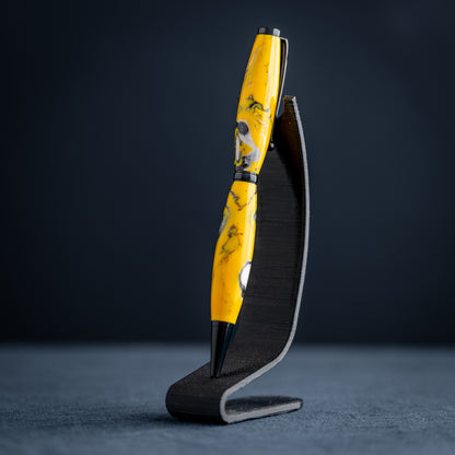 Handmade yellow, black, and white resin swirl ballpoint twist pen on a dark stand against a dark background.