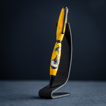 Handmade yellow, black, and white resin swirl ballpoint twist pen on a dark stand against a dark background.
