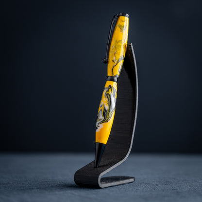 Handmade yellow, black, and white resin swirl ballpoint twist pen on a dark stand against a dark background.