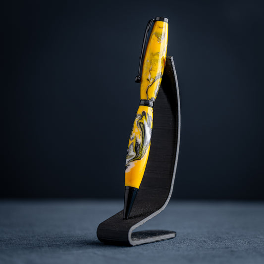 Handmade yellow, black, and white resin swirl ballpoint twist pen on a dark stand against a dark background.