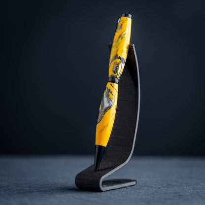 Handmade yellow, black, and white resin swirl ballpoint twist pen on a dark stand against a dark background.