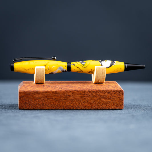 Handmade yellow, black, and white resin swirl ballpoint twist pen on a wooden stand against a dark background.