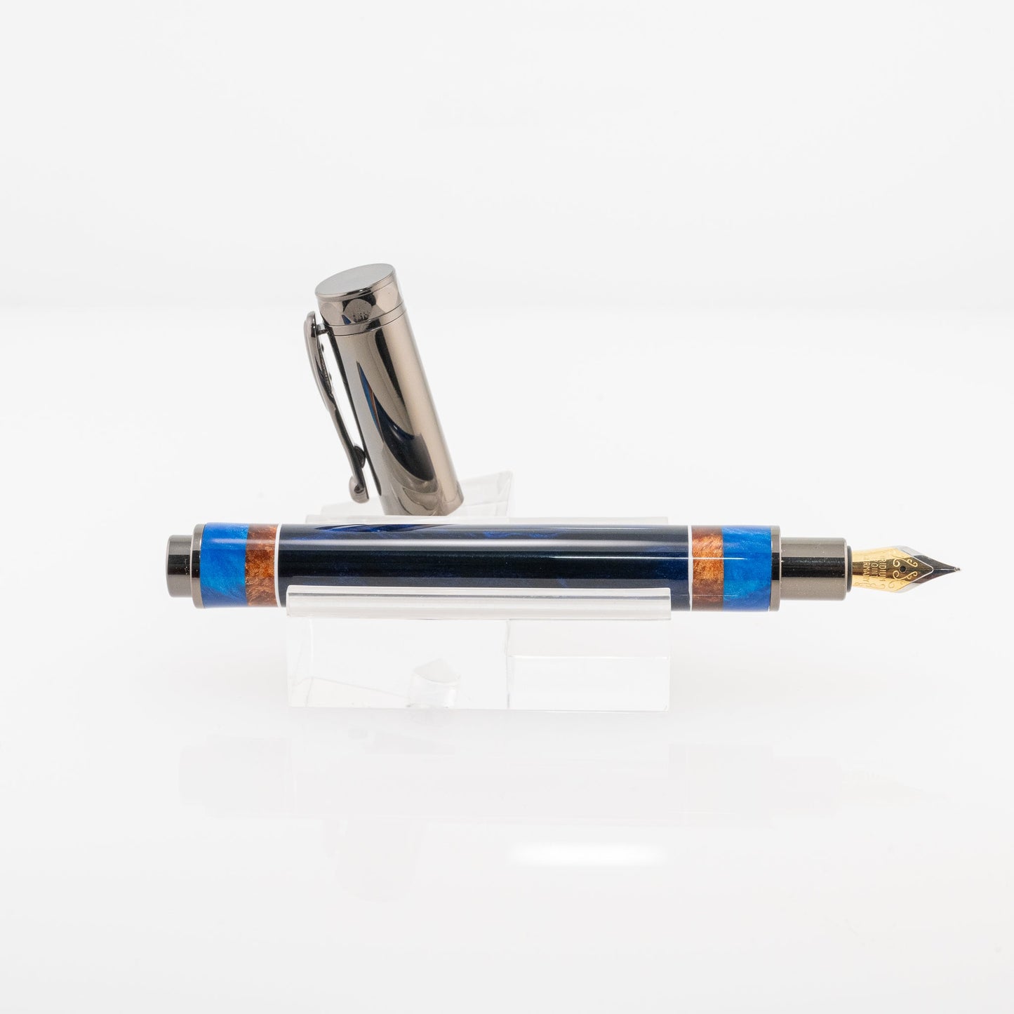 A handmade blue and bronze resin fountain pen rests on a clear stand. The plating is gunmetal and it features a shiny German Iridium nib.
