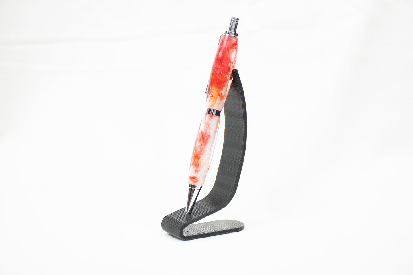 Handmade resin click pen with red translucent swirl dye on white background finished in chrome plating