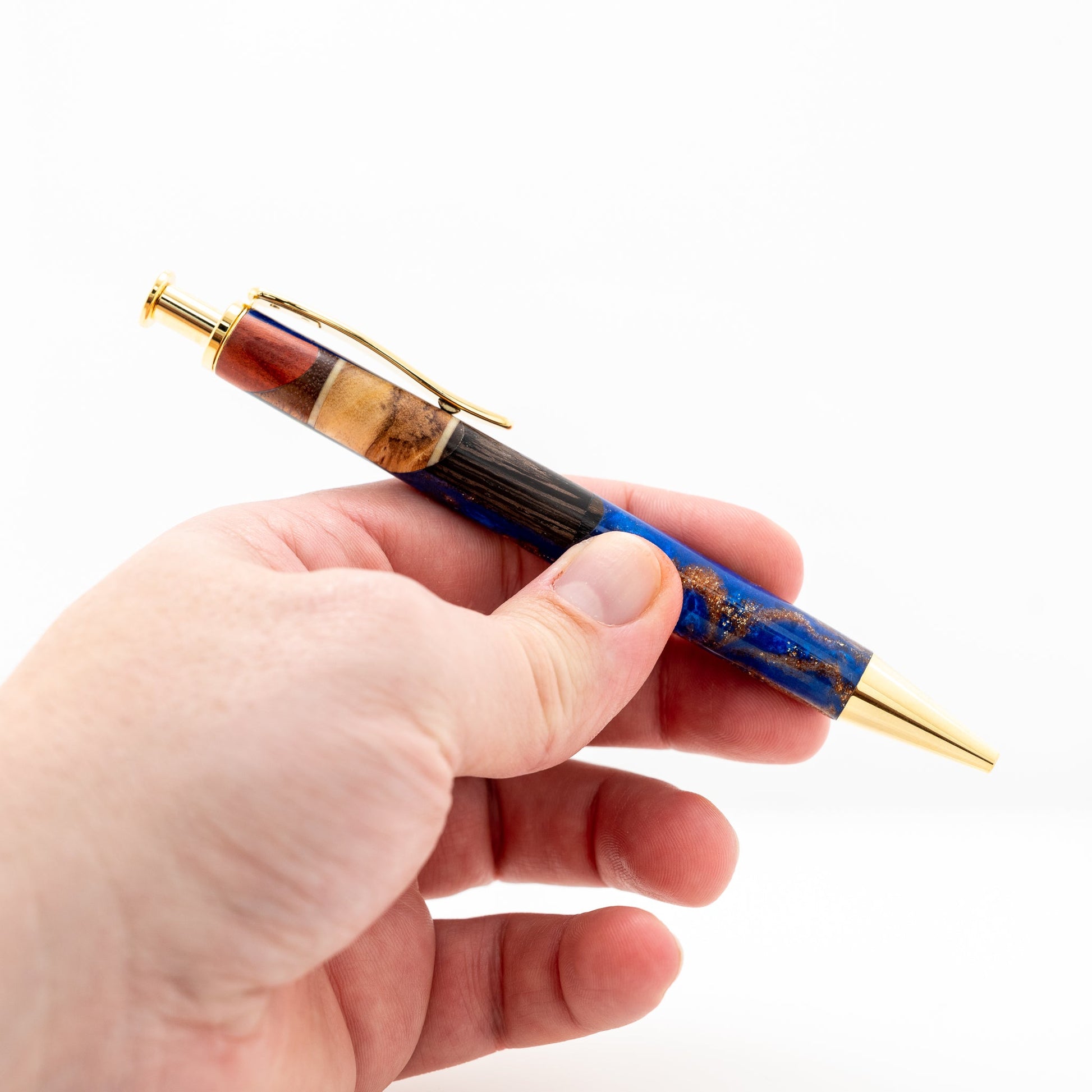 Handmade long click pen with olive wood, wenge, maple and redheart wood suspended in blue sparkle resin with gold plating