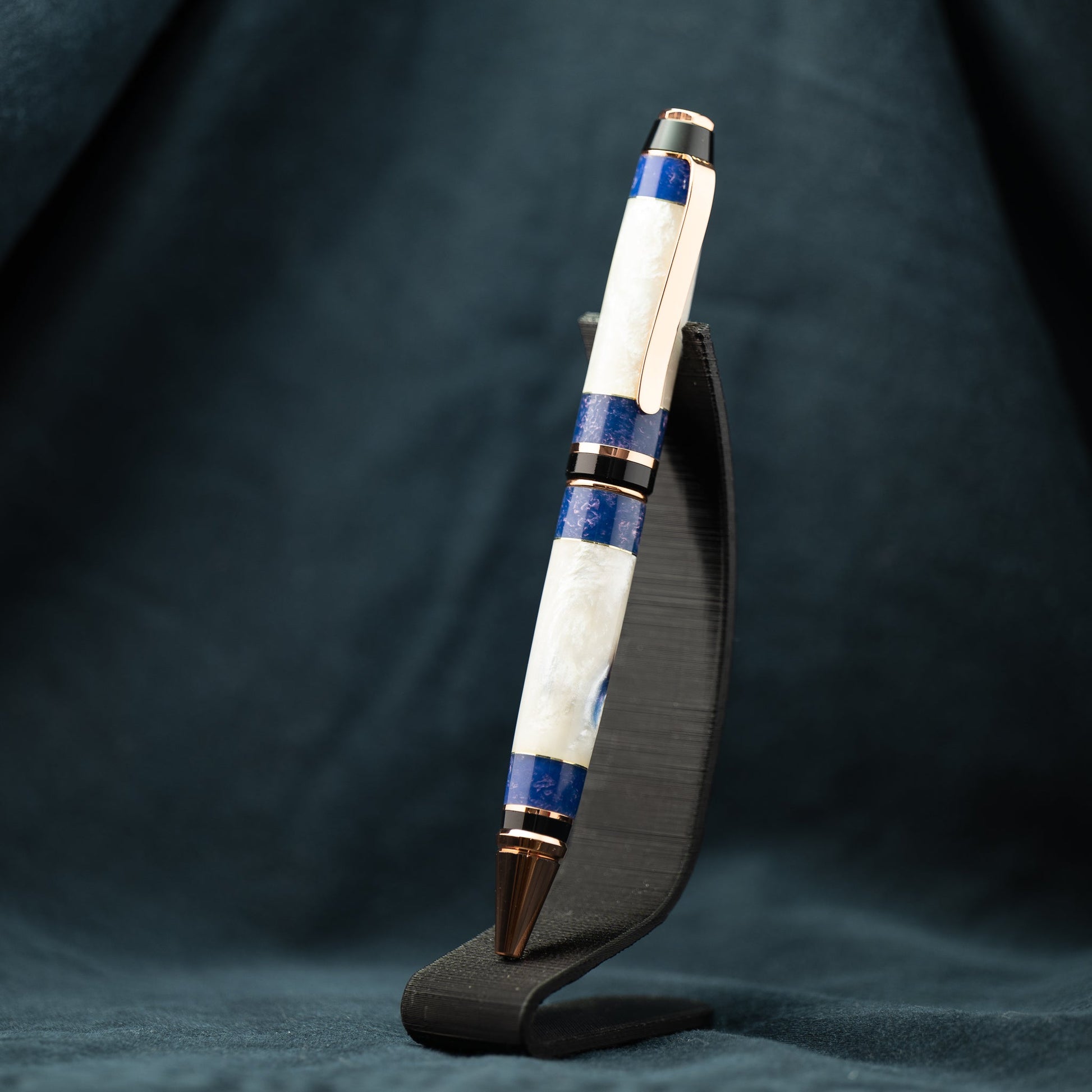 A hanmade white, blue, bronze, and purple resin twist ballpoint pen with bright copper plating.