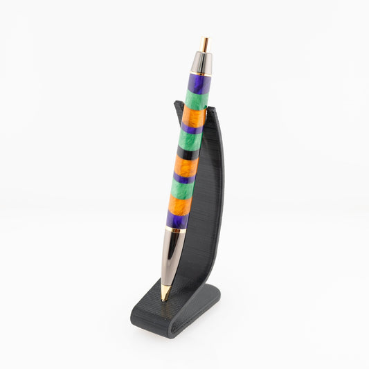 Orange, purple, and green handmade striped resin ballpoint click pen with gold and gunmetal plating on a black stand.