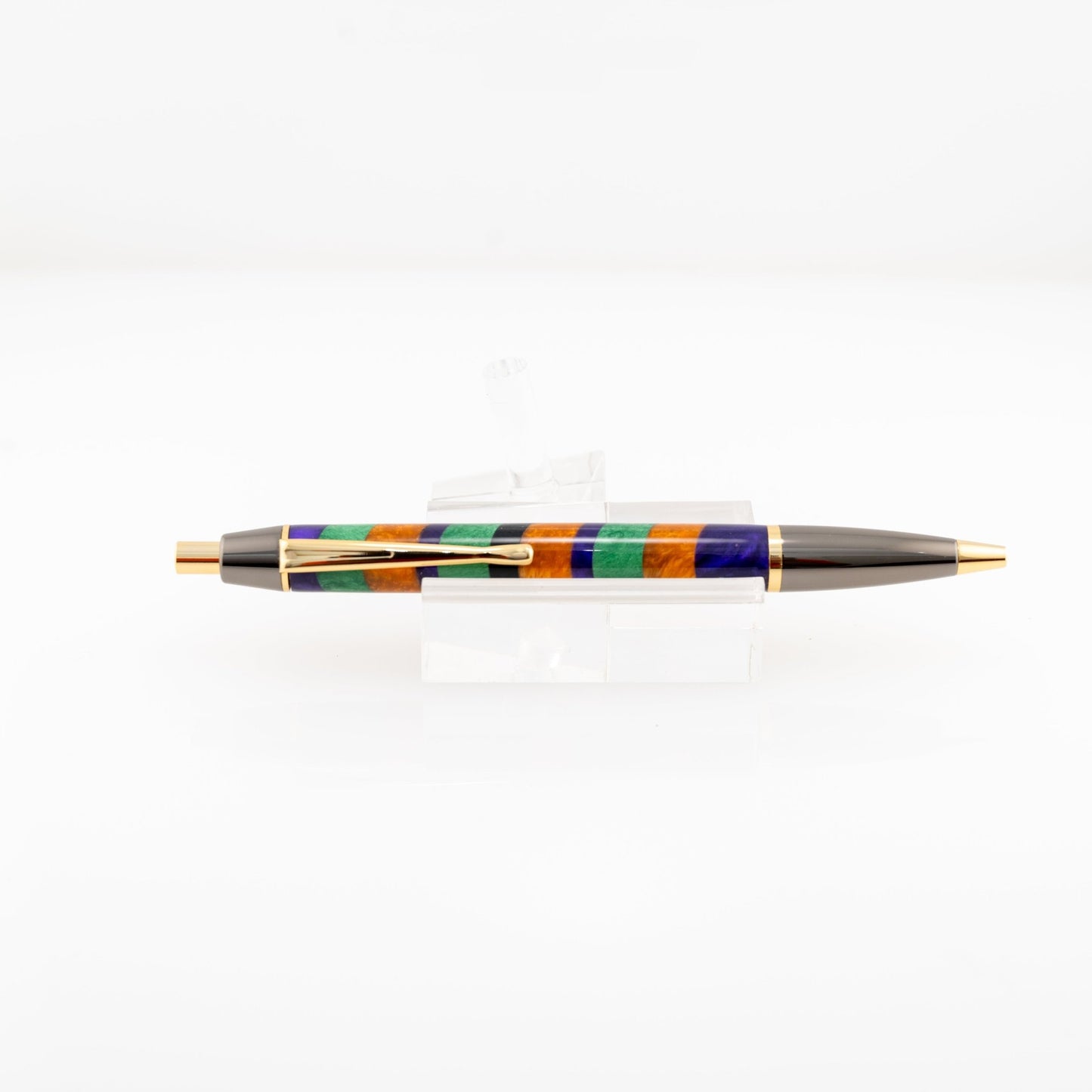 Orange, purple, and green handmade striped resin ballpoint click pen with gold and gunmetal plating on a clear stand.