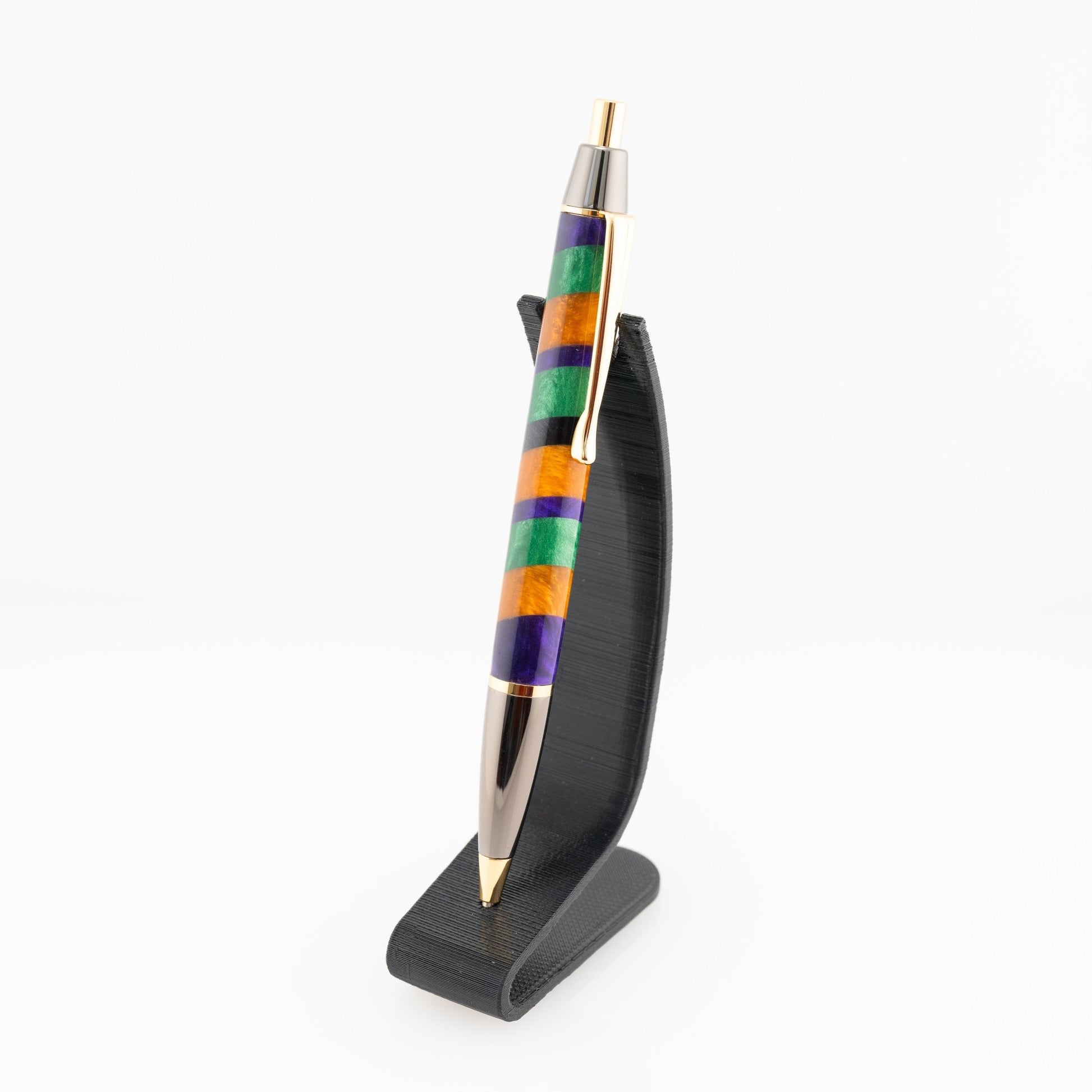 Orange, purple, and green handmade striped resin ballpoint click pen with gold and gunmetal plating on a black stand.