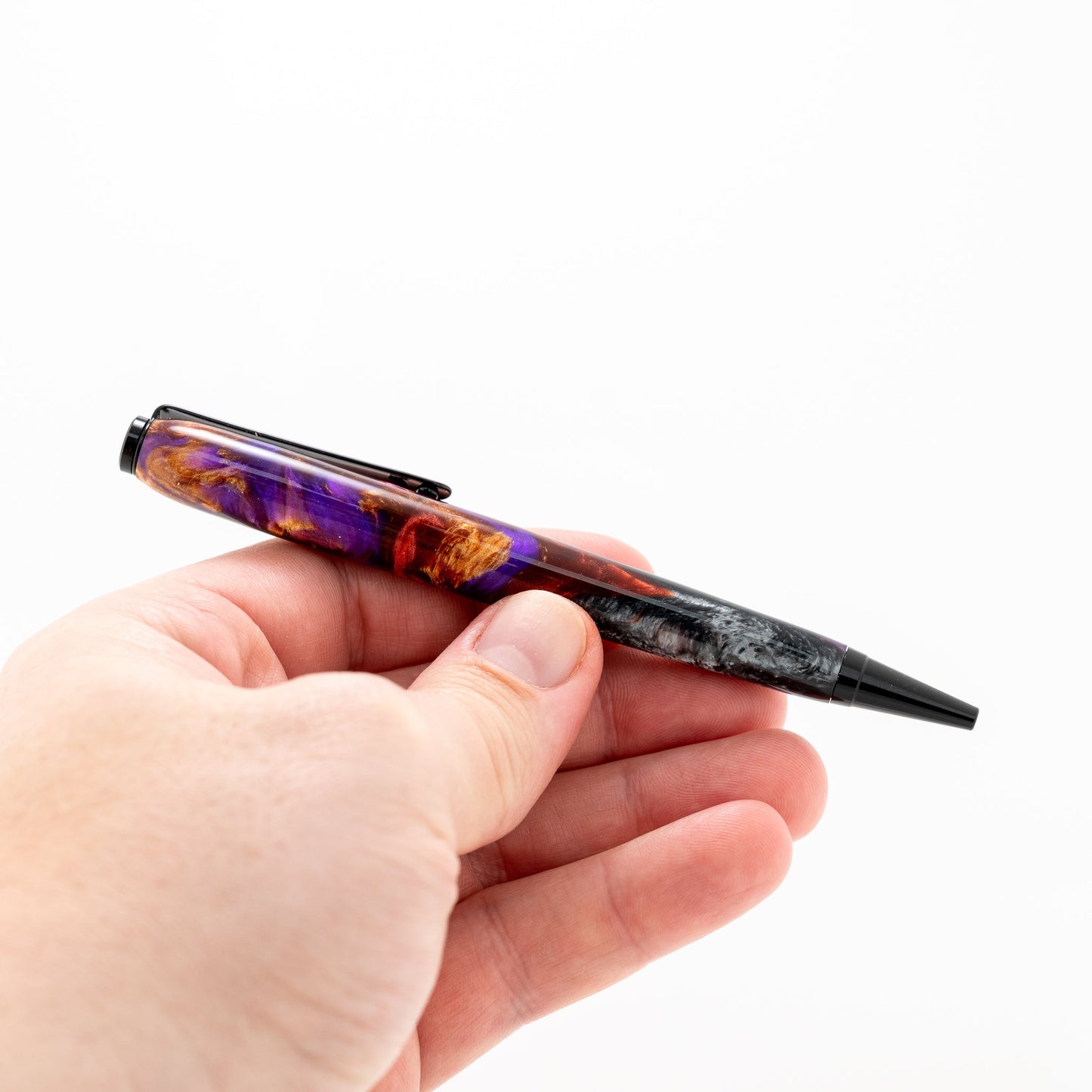 Handmade red, purple, black, grey and bronze swirled resin ballpoint twist pen with black chrome plating held in a hand