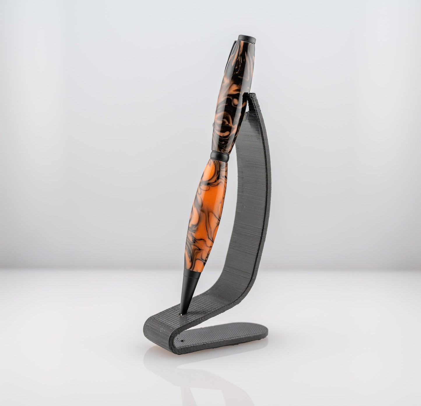 Handmade orange and black resin twist ballpoint pen on a black stand