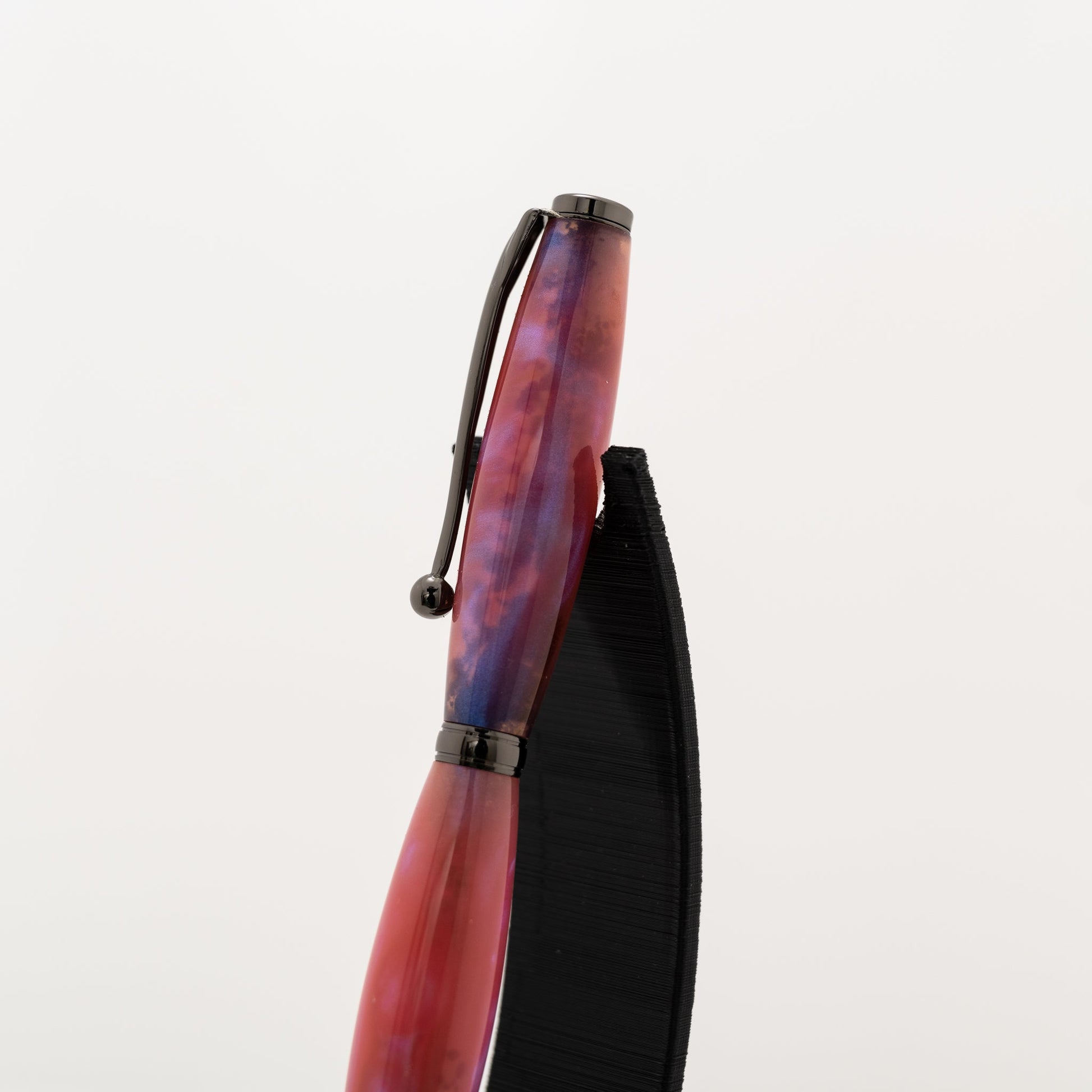 handmade pink and black resin twist ballpoint pen on a black stand