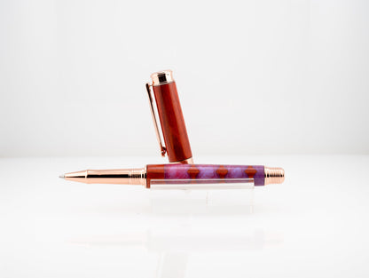 handmade redheart wood and resin rollerball pen with rose gold plating on a black stand
