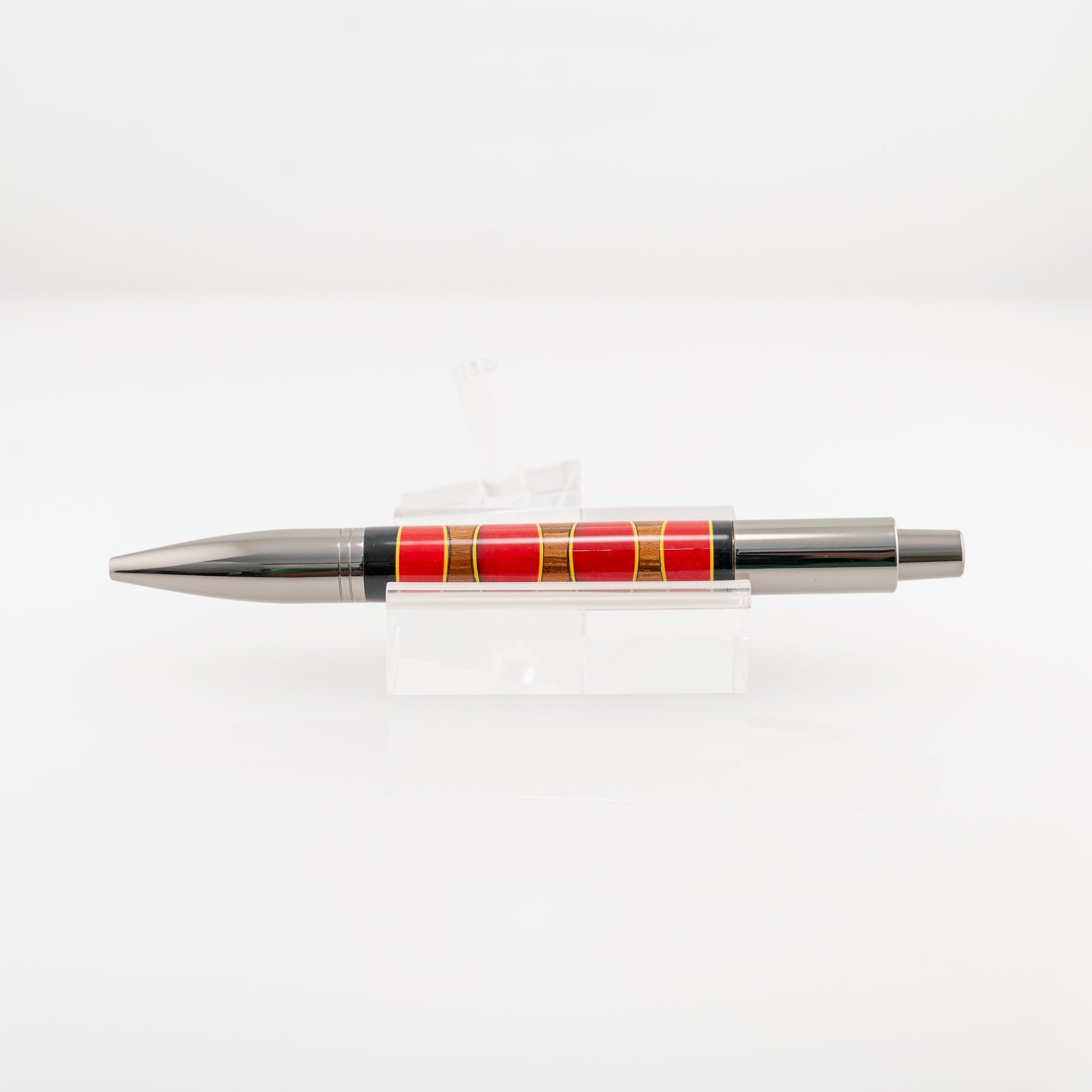 Handmade red and black resin and Canarywood segmented ballpoint click pen on a clear stand.