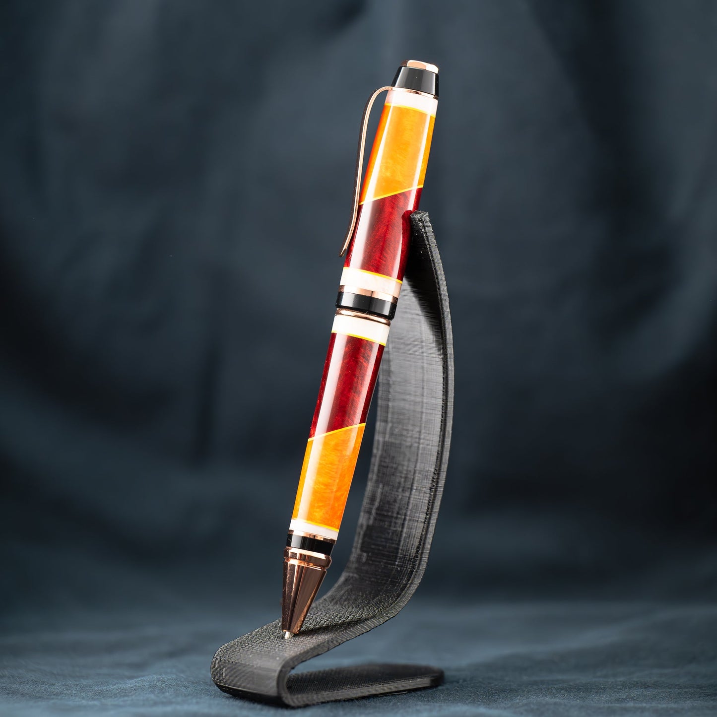 A handmade red, orange, and yellow resin cigar twist ballpoint pen with bright copper plating.