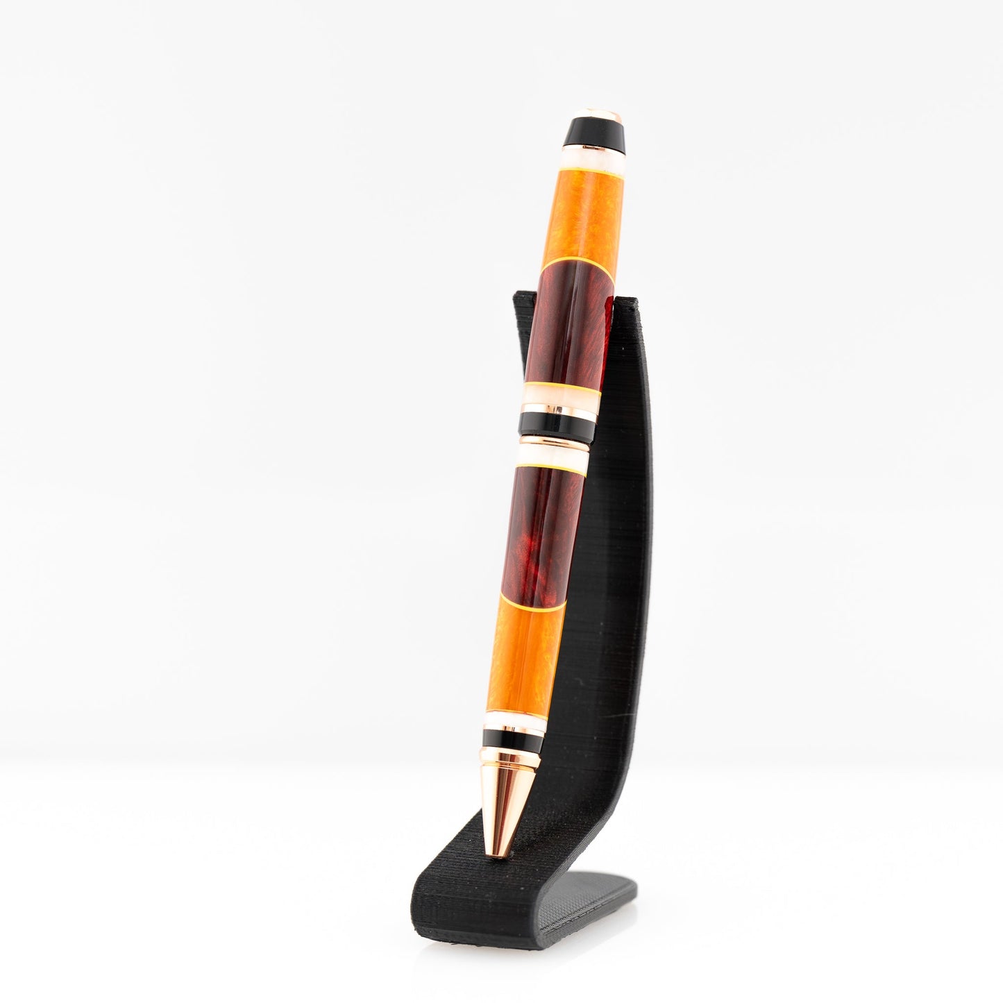 A handmade red, orange, and yellow resin cigar twist ballpoint pen with bright copper plating.