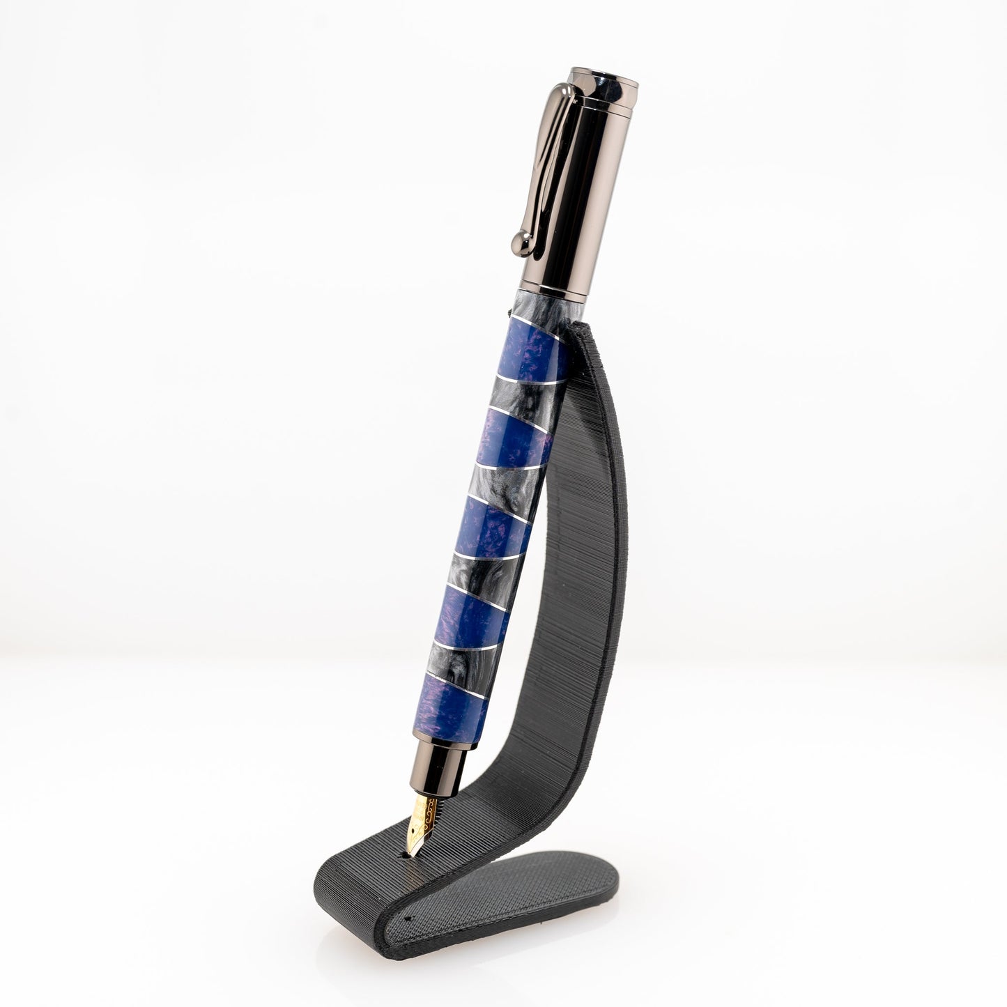 A handmade purple and silver resin and aluminum fountain pen rests on a black stand. The plating is gunmetal and it features a German Iridium nib.