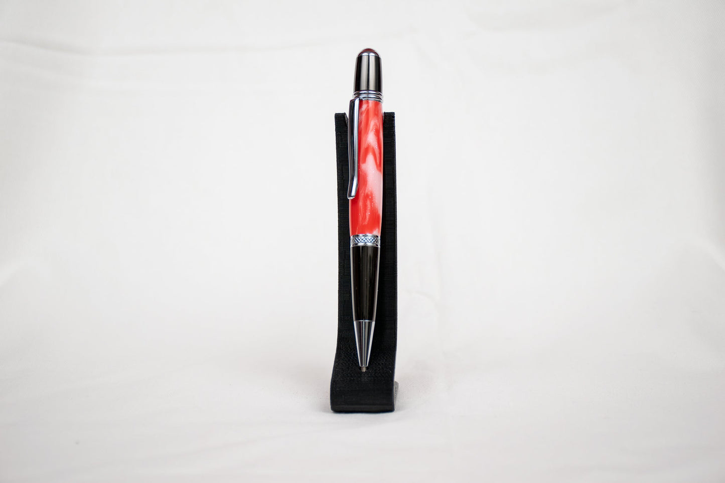 handmade red and white resin ballpoint twist pen with chrome plating on a black stand