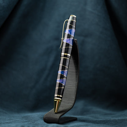 A handmade segmented black, purple, and brass resin ballpoint twist pen with gold plating