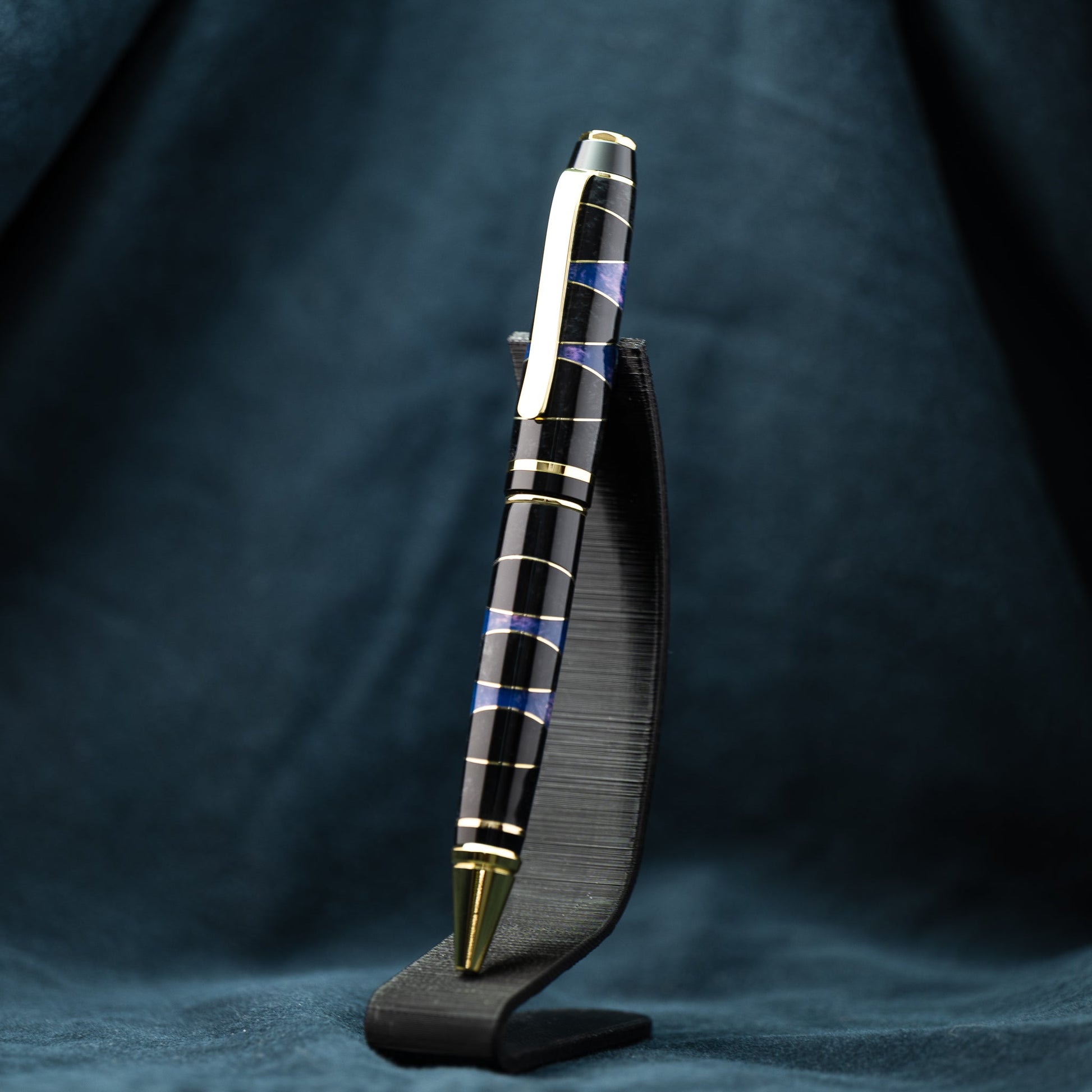 A handmade segmented black, purple, and brass resin ballpoint twist pen with gold plating