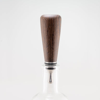 A hanmade Wenge wood bottle stopper rests in a clear bottle. The dropper is stainless steel with three black silicon gaskets.
