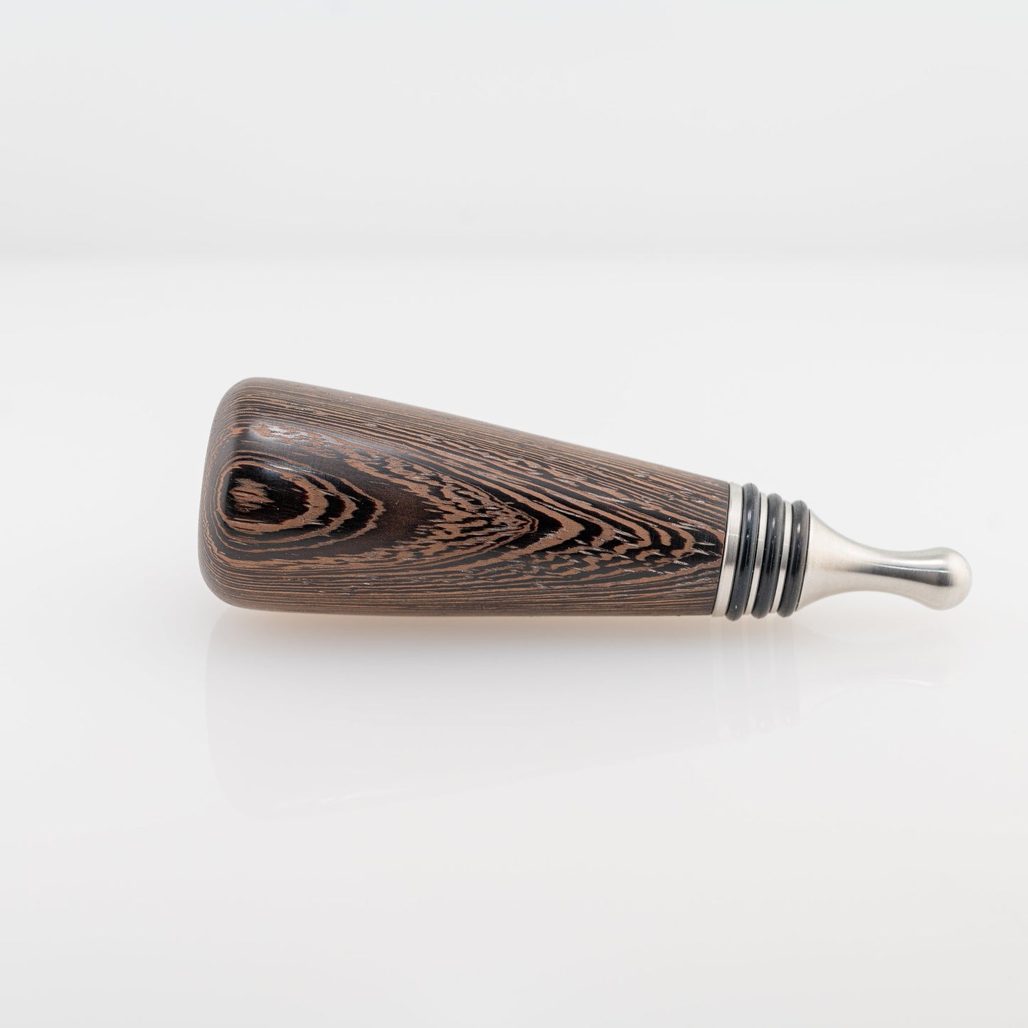 A hanmade Wenge wood bottle stopper rests on its side. The dropper is stainless steel with three black silicon gaskets.